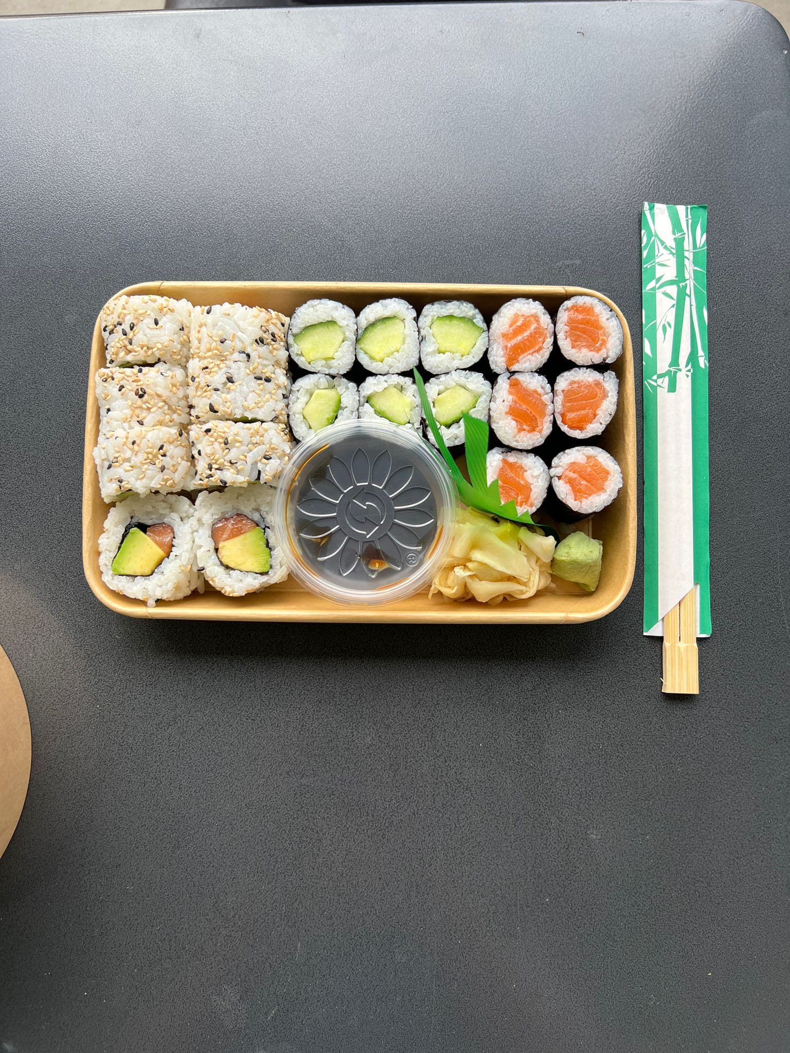 Sushi-Box von oben mit Maki und Inside-Out-Rollen, daneben Stäbchen, auf dunklem Tisch